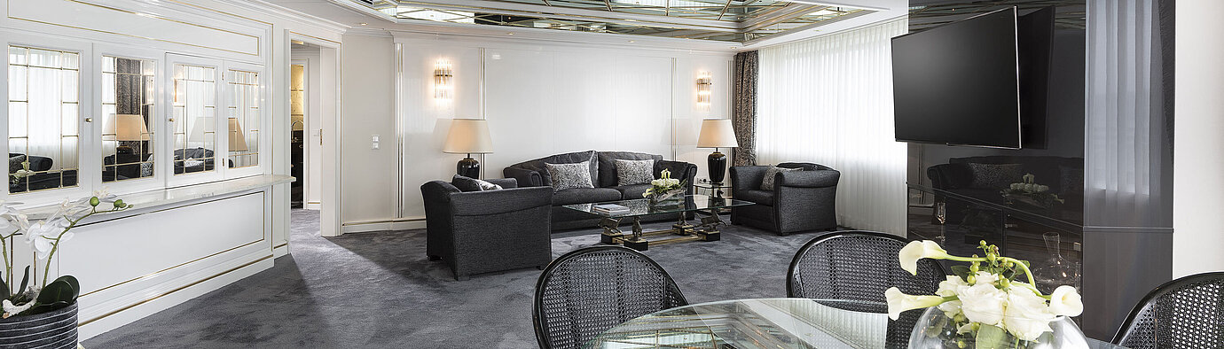 Stilvolles Wohnzimmer der Luxus-Suite im Maritim Hotel Bonn mit Spiegeldecke, modernen Möbeln und einem großen Esstisch.