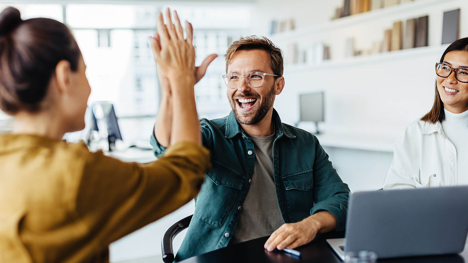 © JLco Julia Amaral - Adobestock.com Zwei Kollegen im Büro geben sich lachend ein High Five als Zeichen erfolgreicher Teamarbeit.