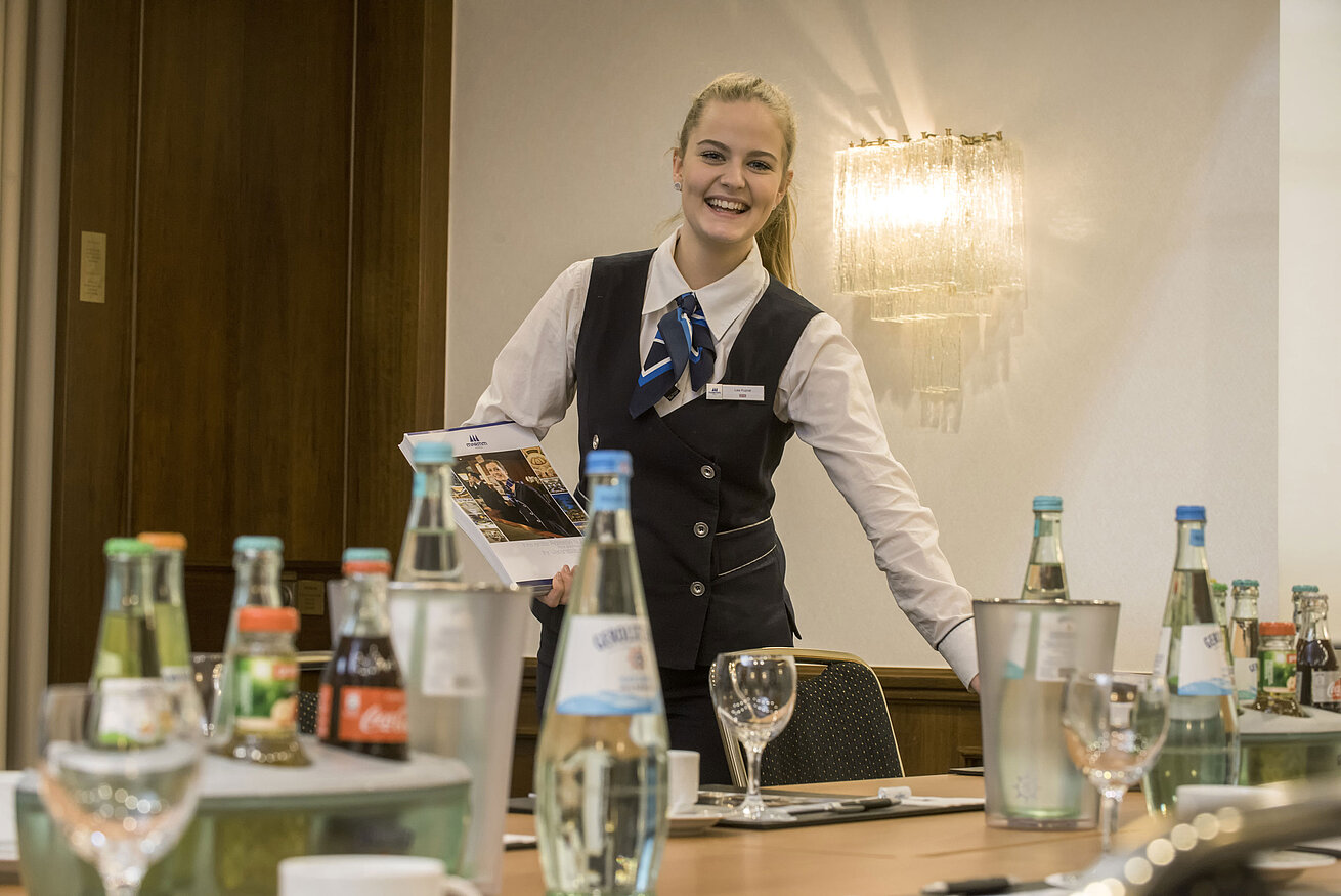 Freundliche Servicemitarbeiterin im Salon Lenné des Maritim Hotels Bonn mit Getränken und Tagungsunterlagen auf dem Tisch.