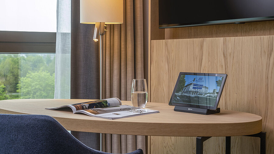 Schreibtisch im Maritim Hotel Ingolstadt mit Tablet, Magazin und Wasserglas, mit Blick auf die Natur durch große Fenster.