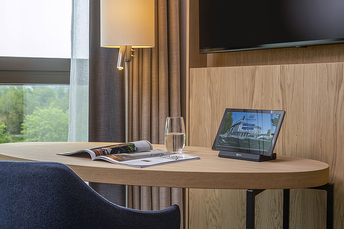 Schreibtisch im Maritim Hotel Ingolstadt mit Tablet, Magazin und Wasserglas, mit Blick auf die Natur durch große Fenster.