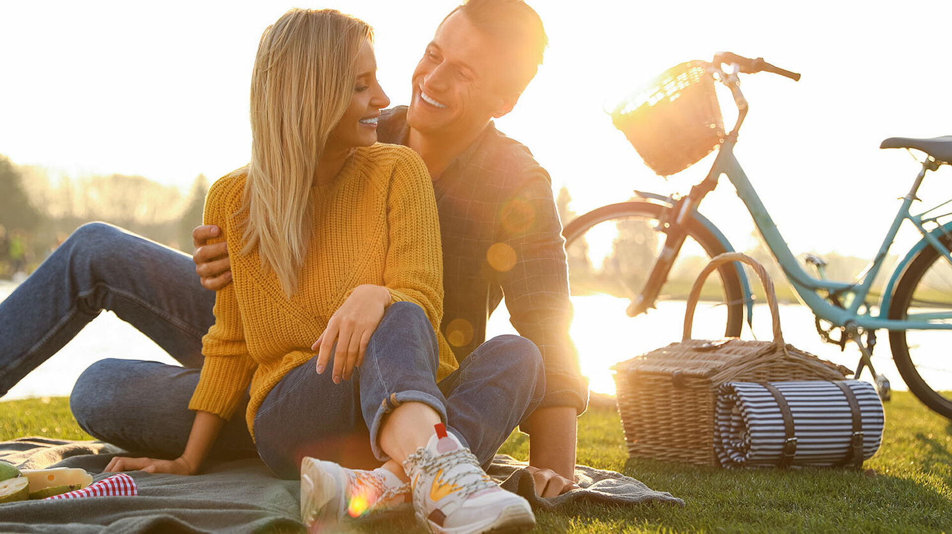 Paar genießt ein Picknick auf einer Wiese neben Fahrrädern bei sonnigem Wetter