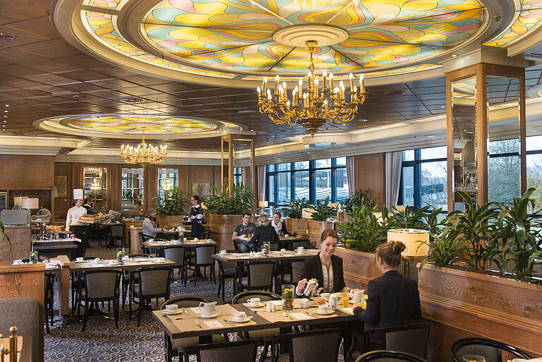 Gäste genießen Frühstück im stilvollen Restaurant mit Kronleuchtern und großen Fenstern im Maritim Hotel Hannover.