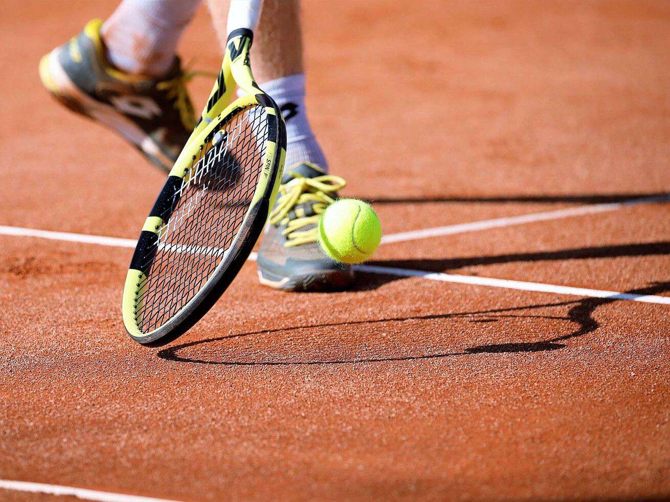 Nahaufnahme eines Tennisschlägers und Tennisballs auf einem roten Sandplatz während eines Matches.