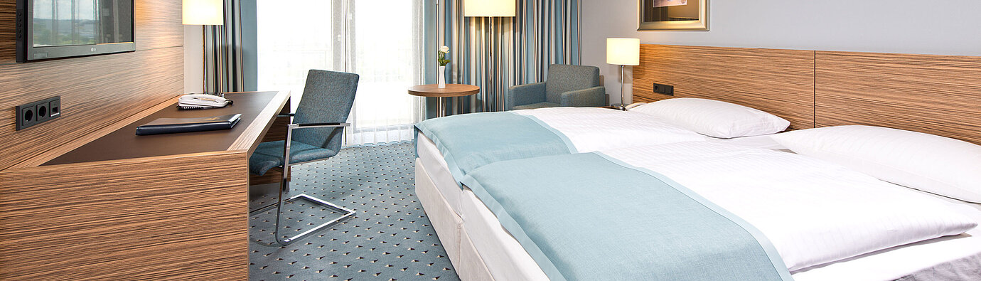 Comfort Zimmer im Maritim Hotel Darmstadt mit modernem Design, Schreibtisch, Sitzbereich und Blick auf große Fenster.