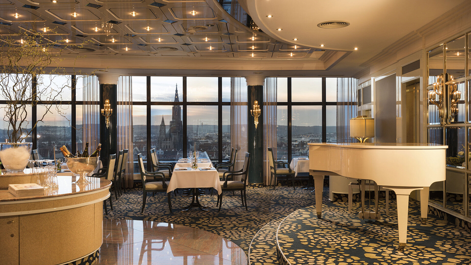 Elegantes Panorama-Restaurant mit Flügel und Blick auf das Ulmer Münster bei Sonnenuntergang