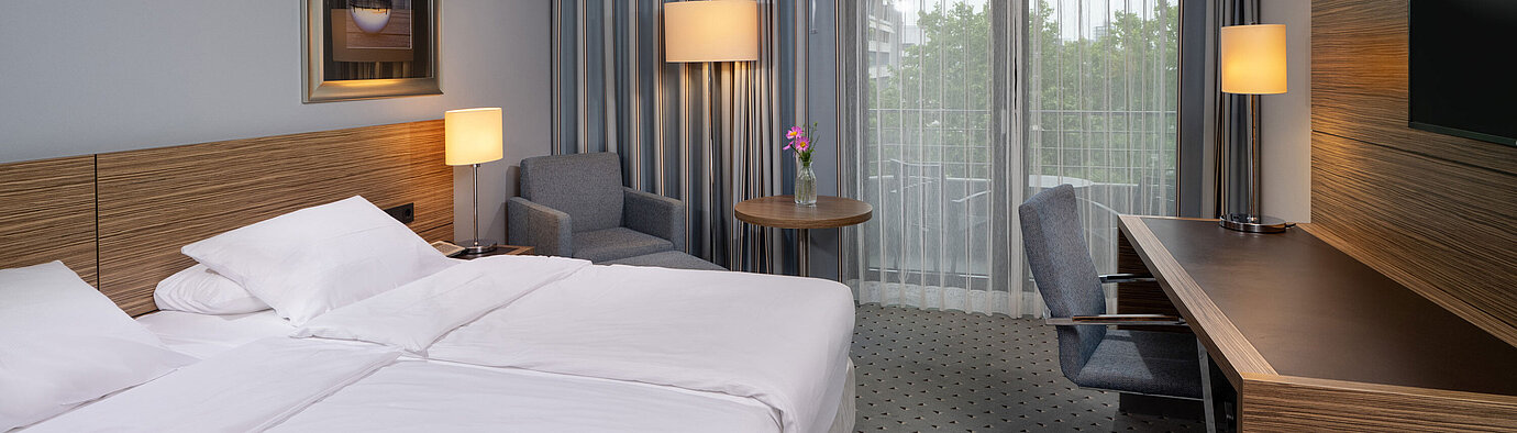 Gesamtansicht des Comfort Zimmers im Maritim Hotel Darmstadt mit Bett, Schreibtisch und Zugang zum Balkon
