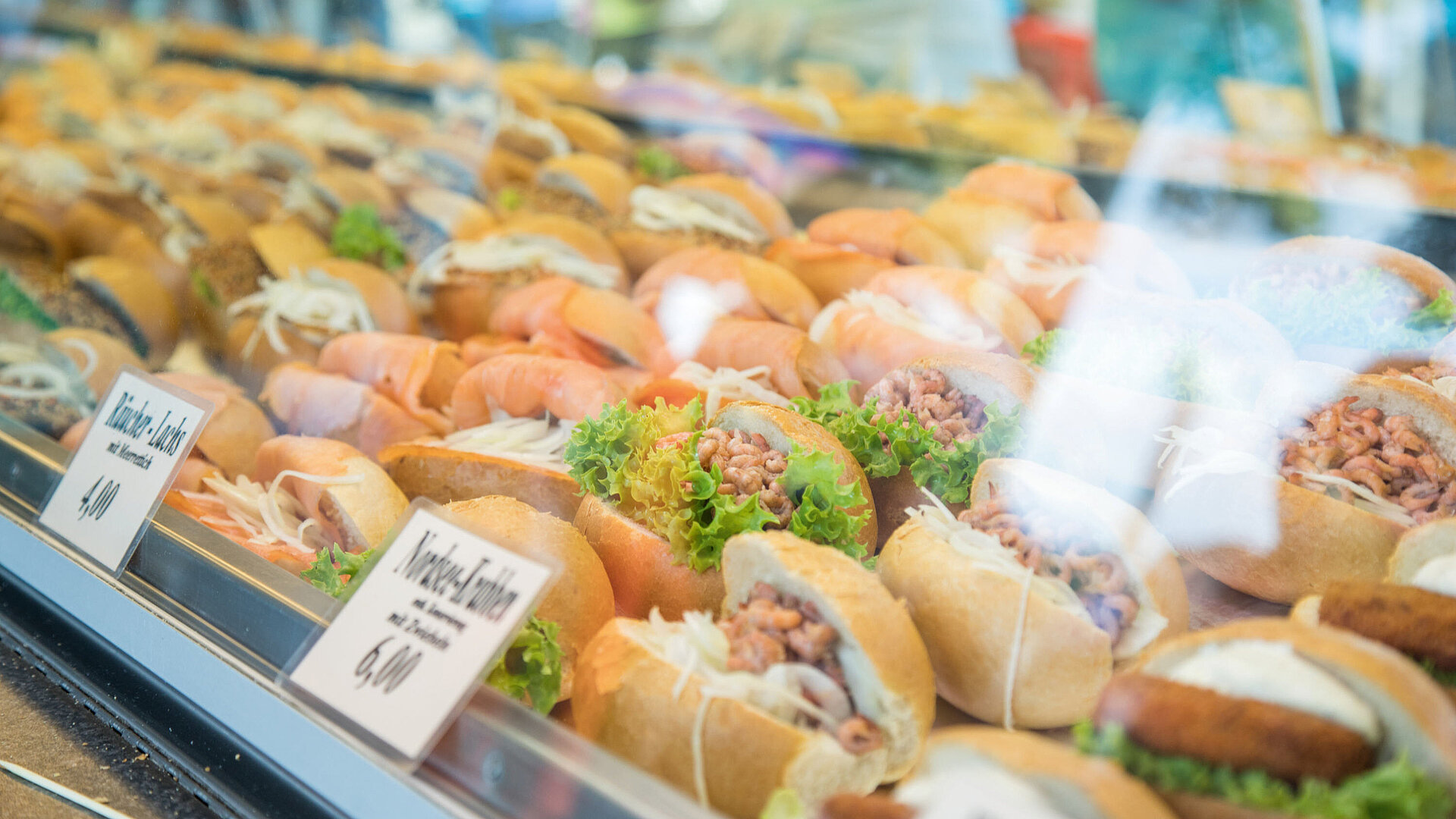 Auswahl frisch belegter Fischbrötchen mit verschiedenen Fischsorten, Salat und weiteren Zutaten in einer Auslage.