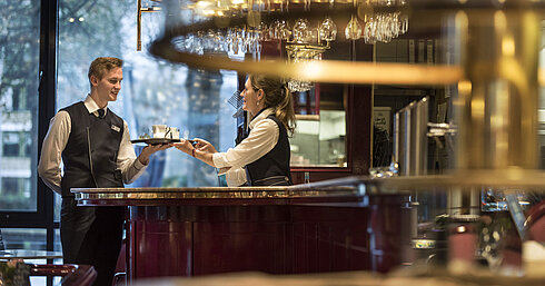 Freundliches Servicepersonal an der Bar der Brasserie im Maritim Hotel Bonn, das Getränkeservice mit einem Lächeln anbietet.