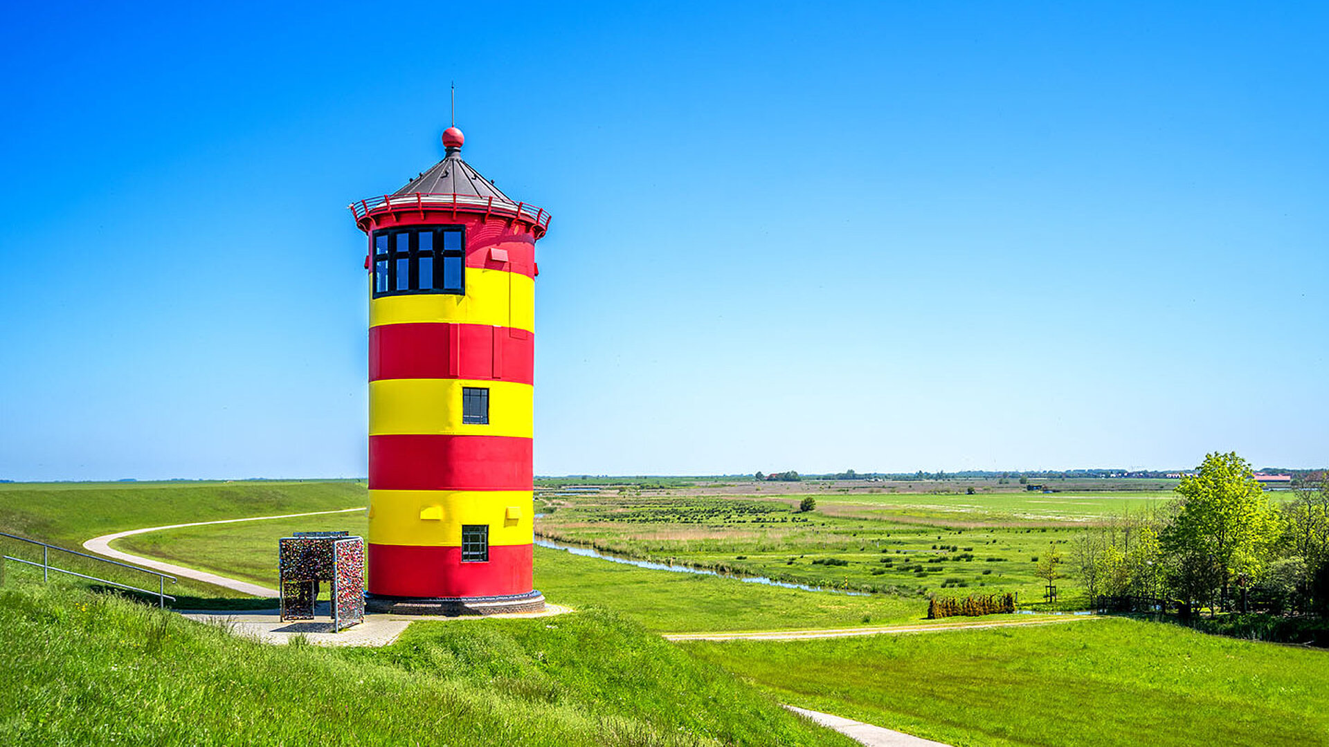 Gelb-rot gestreifter Leuchtturm umgeben von Grün in Pilsum in Ostfriesland 