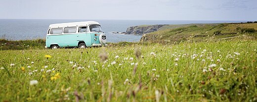 Retro-VW-Bus auf einer Wiese mit Blick auf das Meer und die Küste – perfekter Start ins nächste Abenteuer