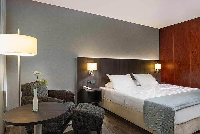 Modernes Doppelzimmer im Maritim Hotel Bremen mit gemütlicher Sitzecke, Beistelltisch, Vase und einladendem Bett.