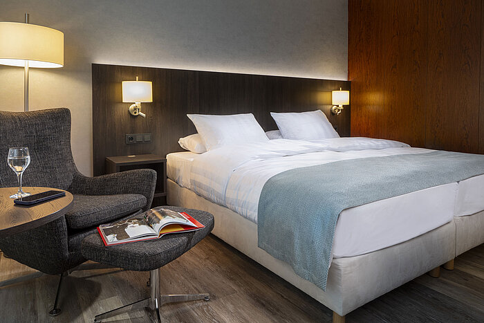 Elegantes Superior Doppelzimmer im Maritim Hotel Bremen mit gemütlichem Sessel, Lesematerial und entspannter Atmosphäre.