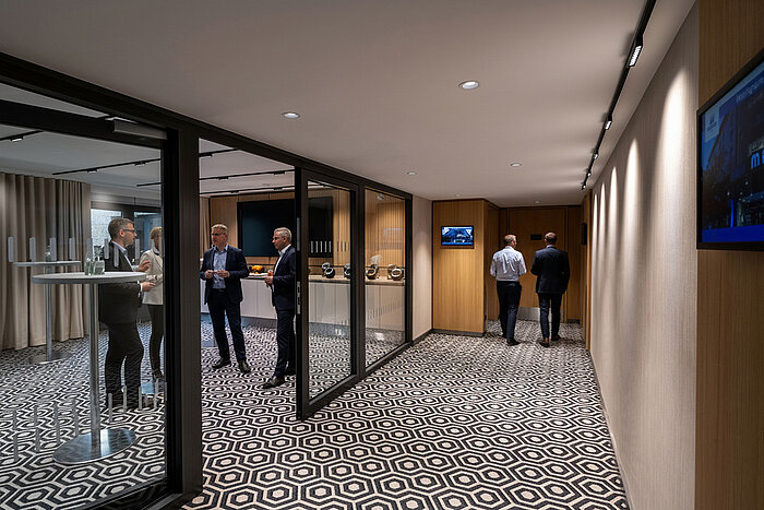 Kaffeepausen-Bereich mit Stehtischen, Kaffeemaschine und Gästen im Gespräch während einer Tagung.