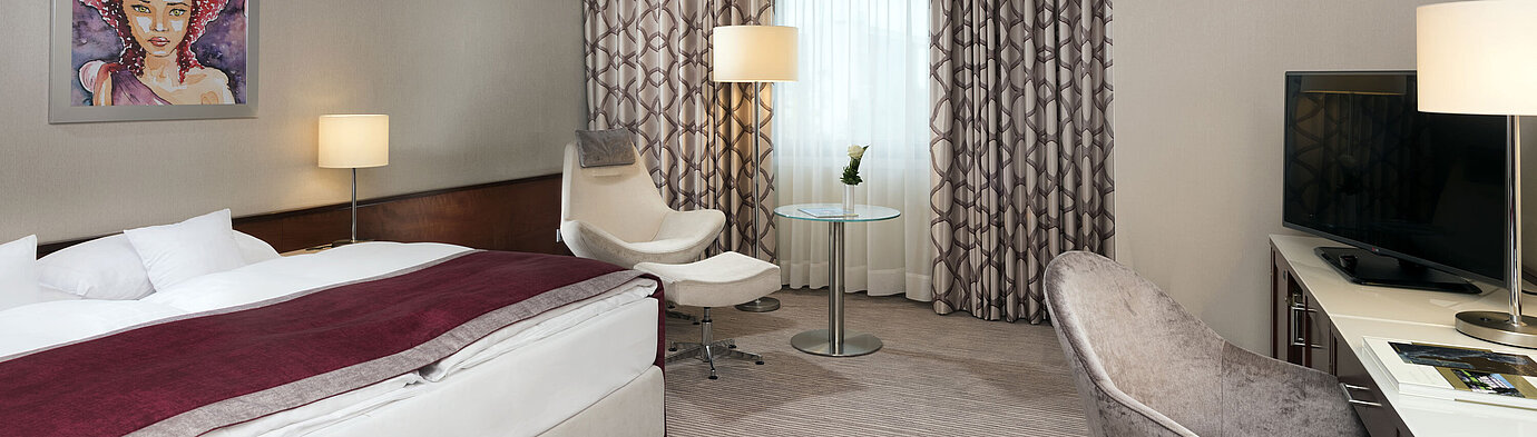 Comfort Zimmer im Maritim Hotel Bonn mit gemütlichem Bett, Sesseln, Schreibtisch und modernen Vorhängen.