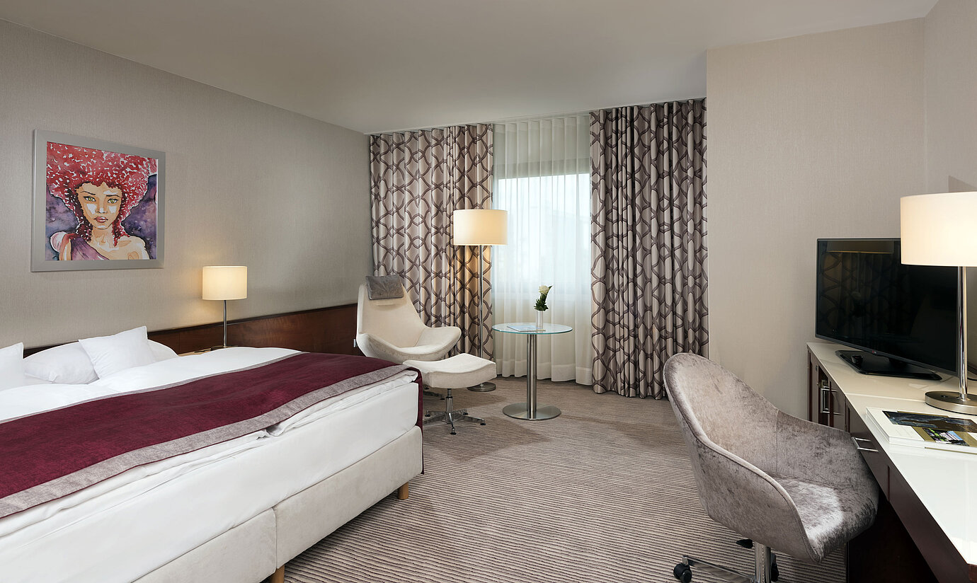 Comfort Zimmer im Maritim Hotel Bonn mit gemütlichem Bett, Sesseln, Schreibtisch und modernen Vorhängen.