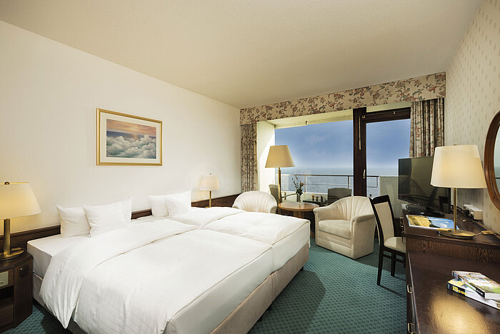 Modernes Hotelzimmer im Maritim Seehotel Timmendorfer Strand mit Meerblick vom Balkon, Doppelbett und Sitzbereich.