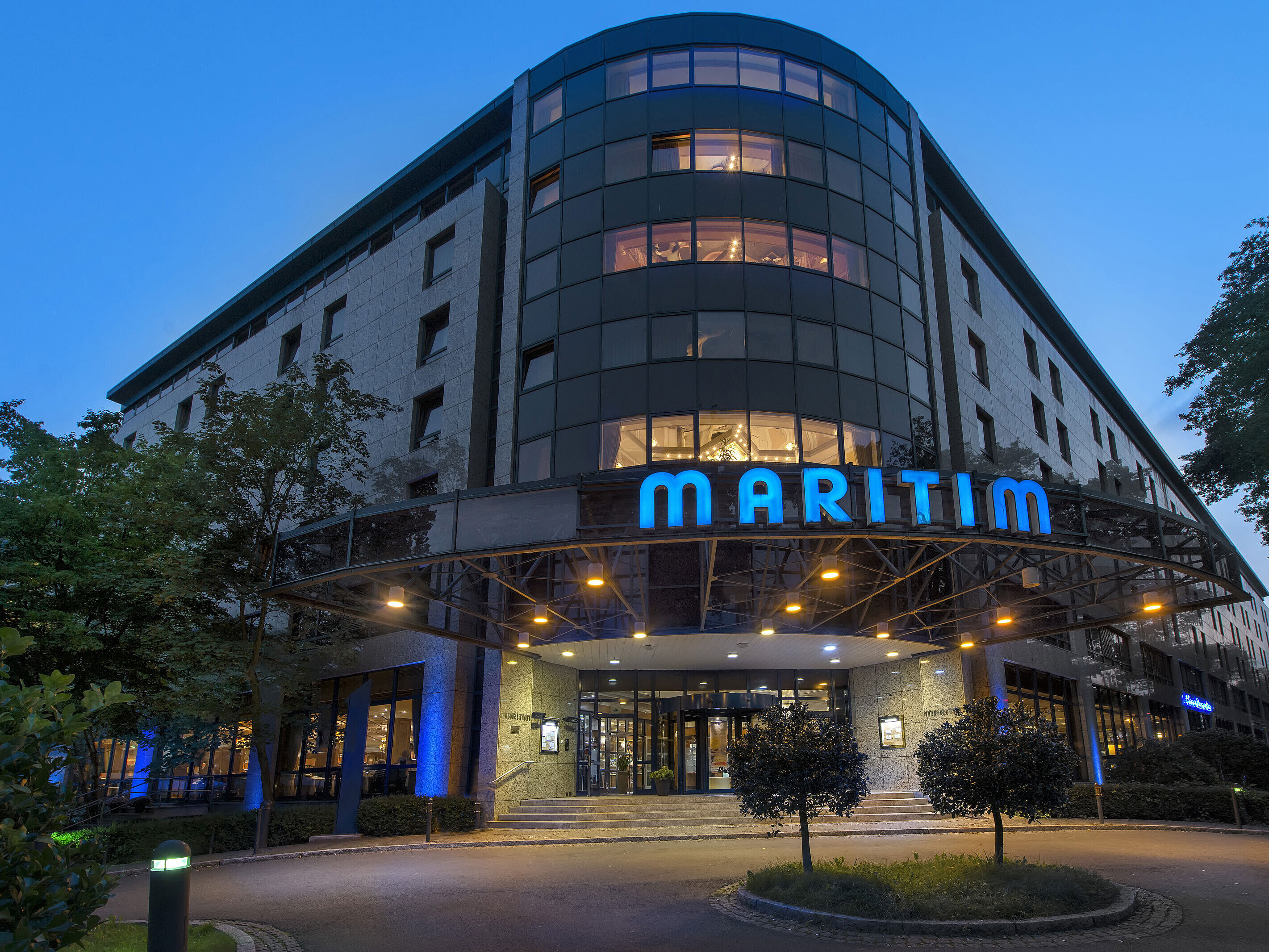 Außenansicht des Maritim Hotel Bremen bei Dämmerung, beleuchtetes Logo und moderne Architektur.
