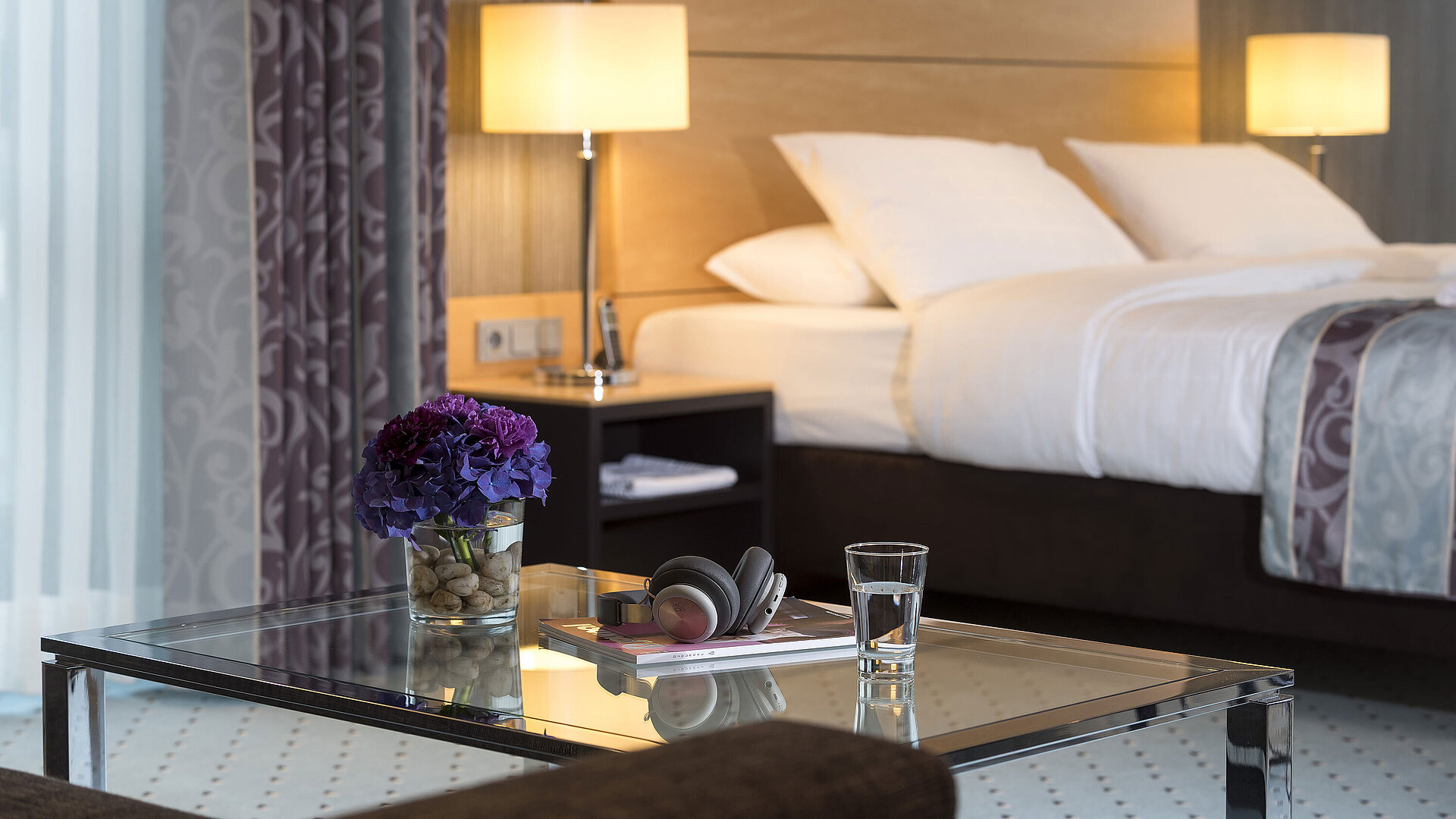 Detailaufnahme der Master Suite im Maritim Hotel Düsseldorf mit einem Glas, Kopfhörern und Blumen auf einem Glastisch.