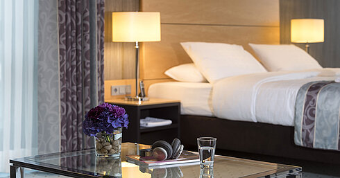 Detailaufnahme der Master Suite im Maritim Hotel Düsseldorf mit einem Glas, Kopfhörern und Blumen auf einem Glastisch.