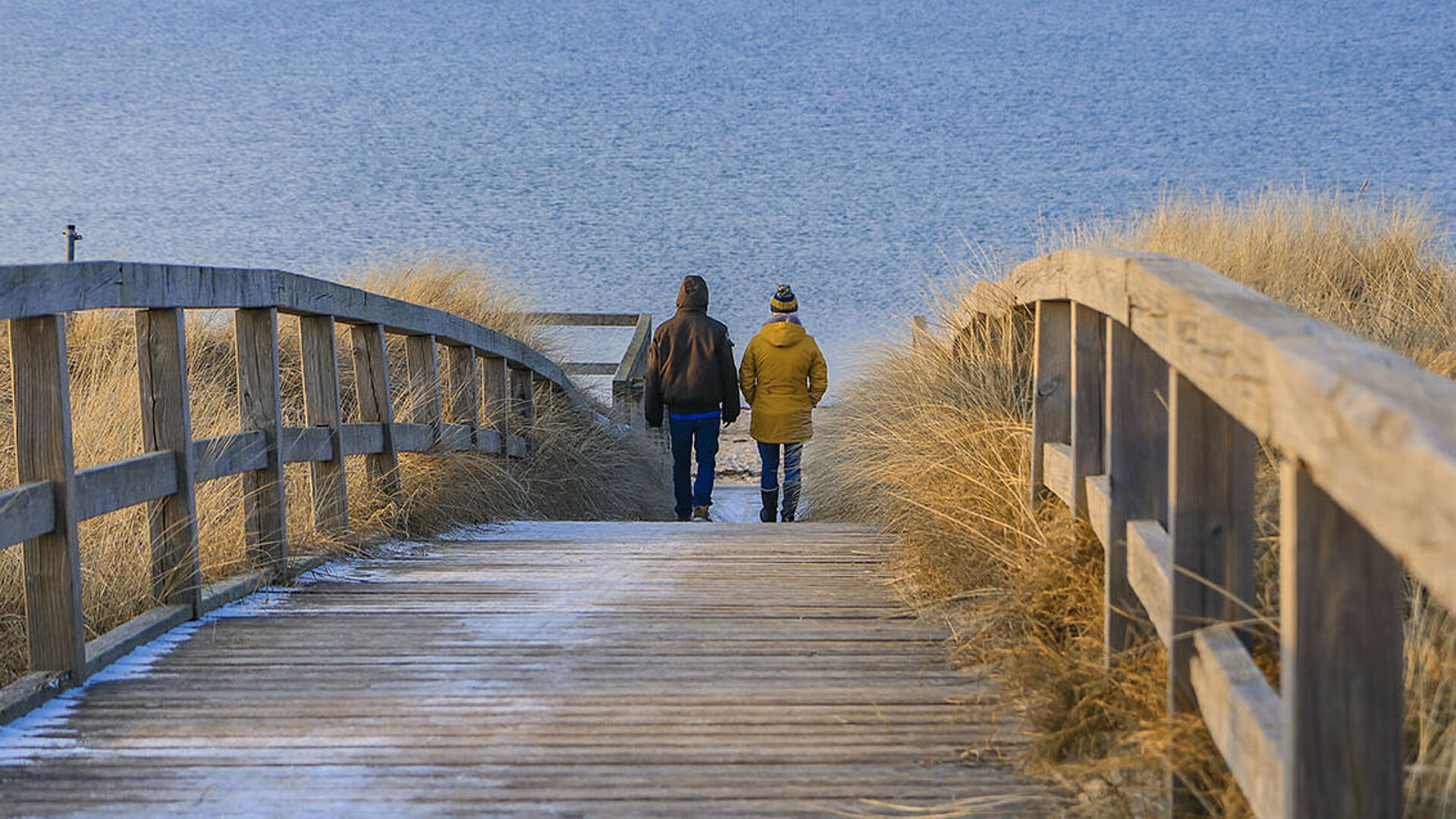 Paar beim Winterspaziergang am Strand über Holzsteg Richtung Meer