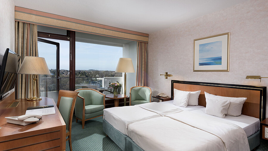 Comfort Zimmer im Maritim Seehotel Timmendorfer Strand mit zwei Betten, Sitzecke, Schreibtisch und Balkon mit Aussicht.