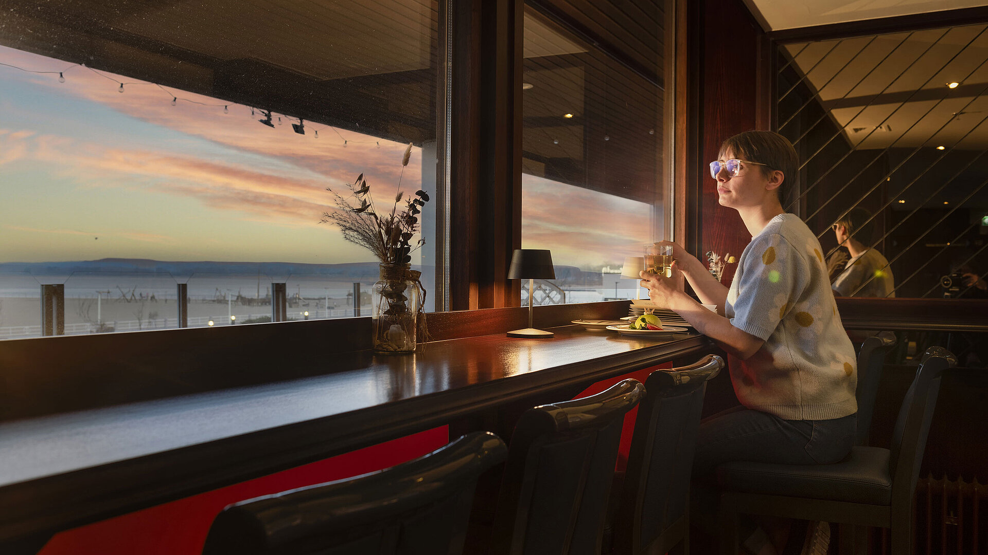 Ostsee Pub Gast sitzt mit Getränk am Fenster und blickt auf den Sonnenuntergang im Maritim Hotel Travemünde