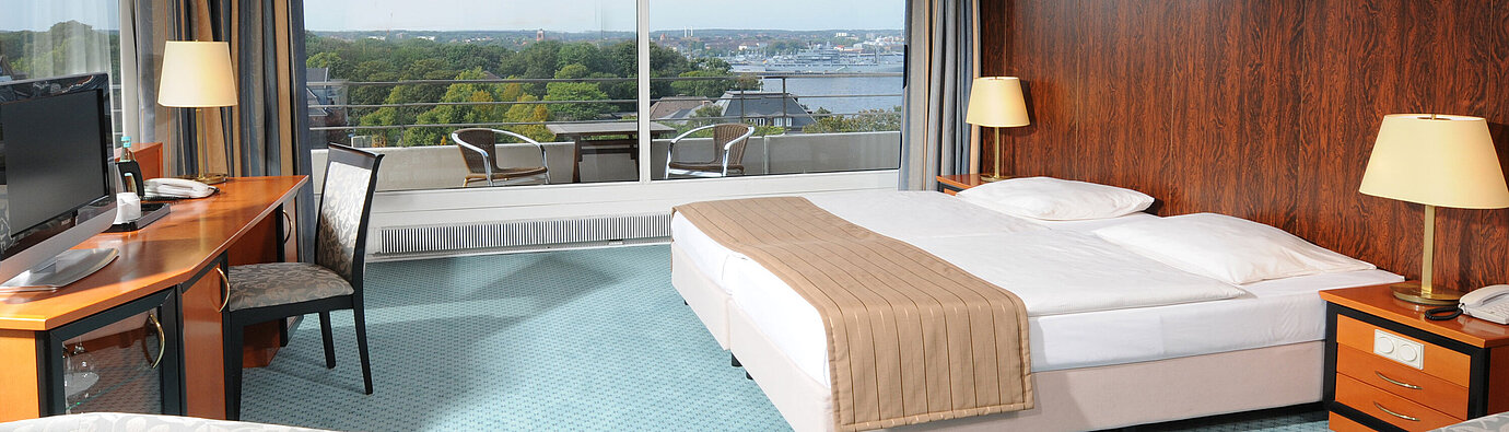 Comfort Doppelzimmer Großzügiges Hotelzimmer mit Doppelbett, Sitzbereich und weitem Ausblick auf Kiel durch die große Fensterfront.