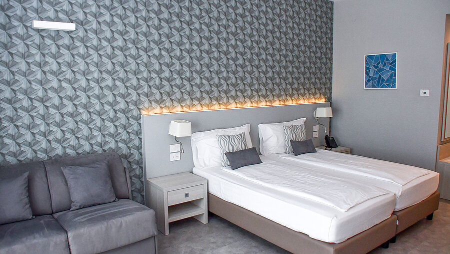 Großzügiges Zimmer im Maritim Resort Calabria mit Twin-Bett, Sofa und stilvoller Wandgestaltung