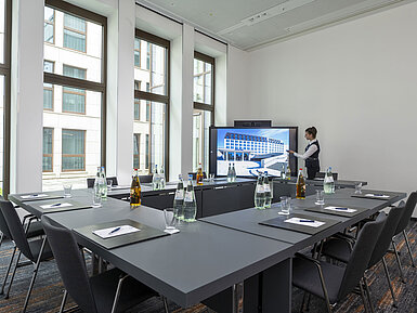 Kompakter Meetingraum im Maritim Hotel Ingolstadt mit großem Bildschirm, moderner Technik und Tageslicht.