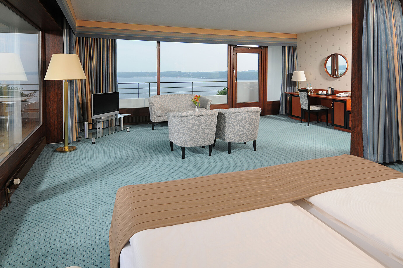 Junior Suite im Maritim Hotel Kiel, mit Sitzecke, Schreibtisch, TV und großer Fensterfront mit Meerblick.