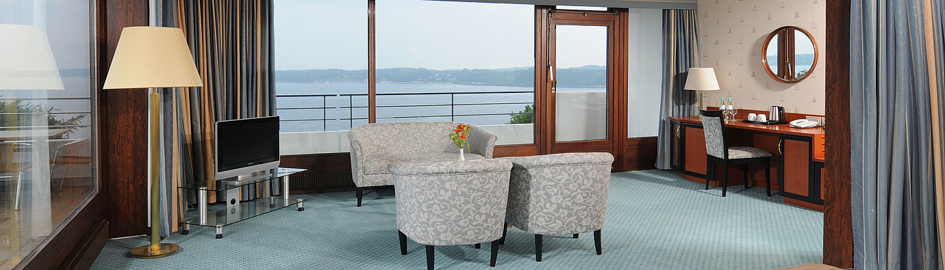 Junior Suite im Maritim Hotel Kiel, mit Sitzecke, Schreibtisch, TV und großer Fensterfront mit Meerblick.
