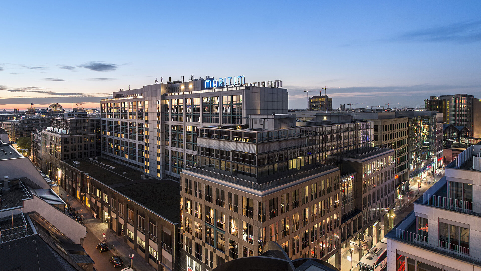 Blick auf das Maritim proArte Hotel Berlin bei Dämmerung, umgeben von modernen Gebäuden im Herzen Berlins.