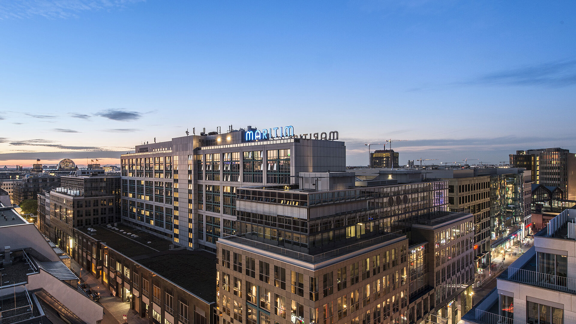 Blick auf das Maritim proArte Hotel Berlin bei Dämmerung, umgeben von modernen Gebäuden im Herzen Berlins.
