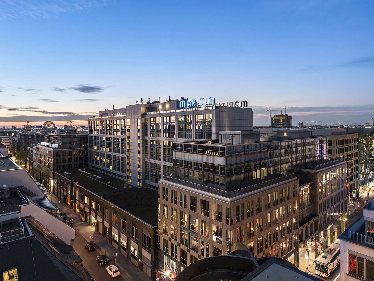 Blick auf das Maritim proArte Hotel Berlin bei Dämmerung, umgeben von modernen Gebäuden im Herzen Berlins.