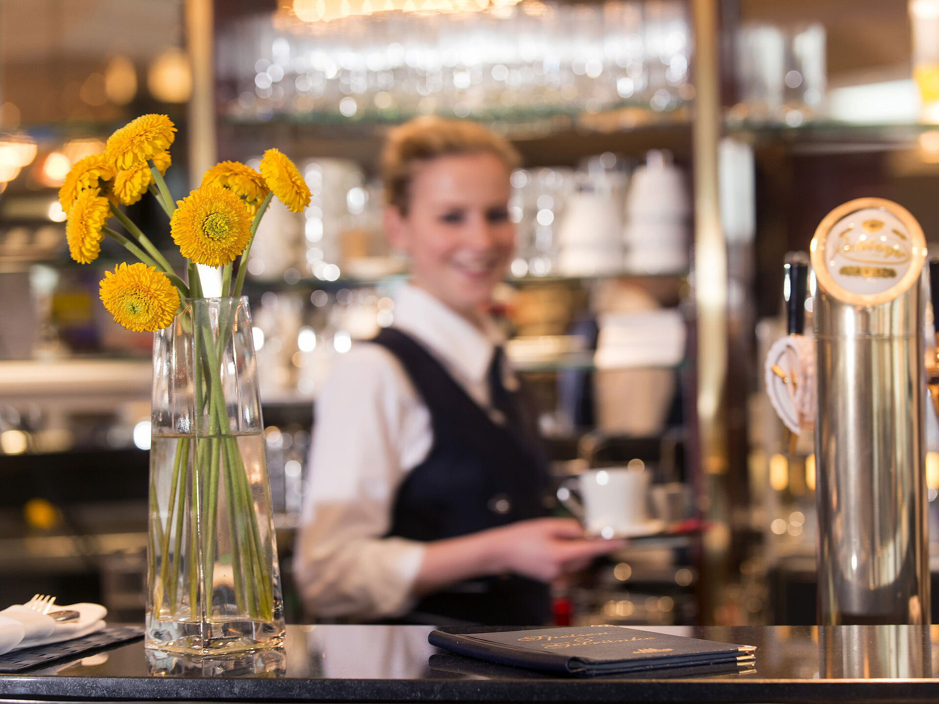 Maritim Service Freundliche Servicekraft an der Bar im Maritim Hotel Stuttgart mit gelben Blumen im Vordergrund