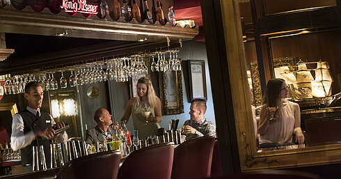 Stimmungsvolle Bar im Maritim Hotel Kiel mit Gästen, die Cocktails genießen, während der Barkeeper einen Drink mixt.