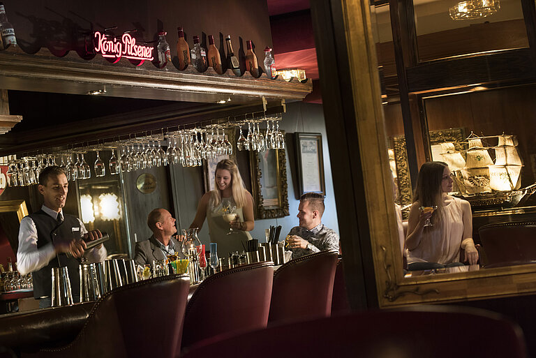 Stimmungsvolle Bar im Maritim Hotel Kiel mit Gästen, die Cocktails genießen, während der Barkeeper einen Drink mixt.