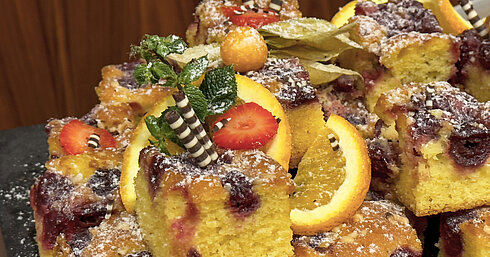 Fruchtiger Kuchen mit Kirschen und Orangenscheiben, dekoriert mit Minze und Schokoröllchen.