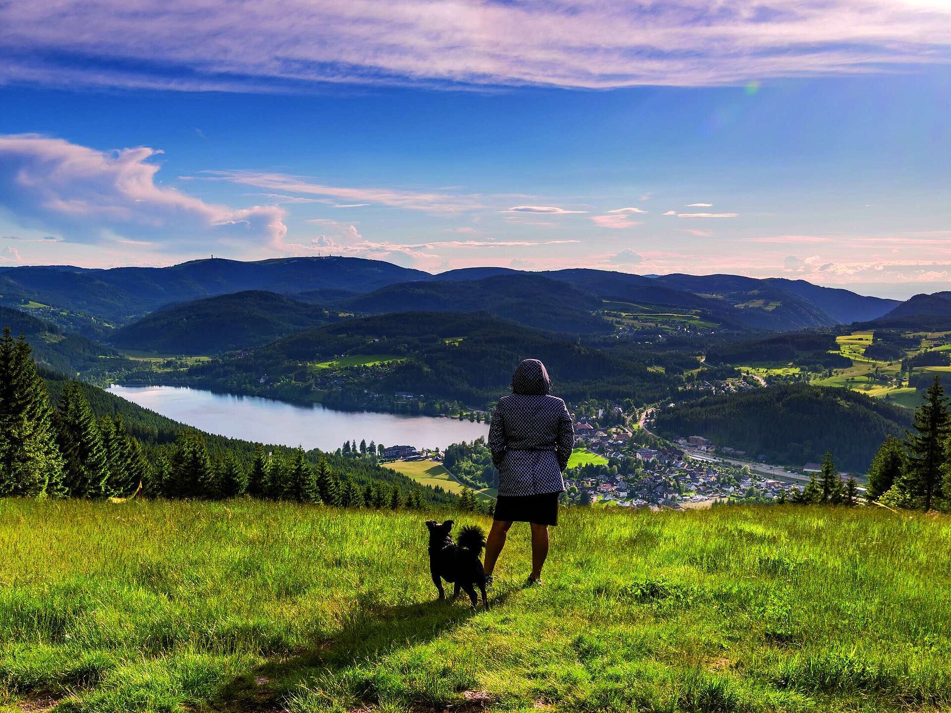Frau mit Hund genießt den Ausblick auf den Titisee und die Landschaft des Schwarzwalds vom Hochfirst