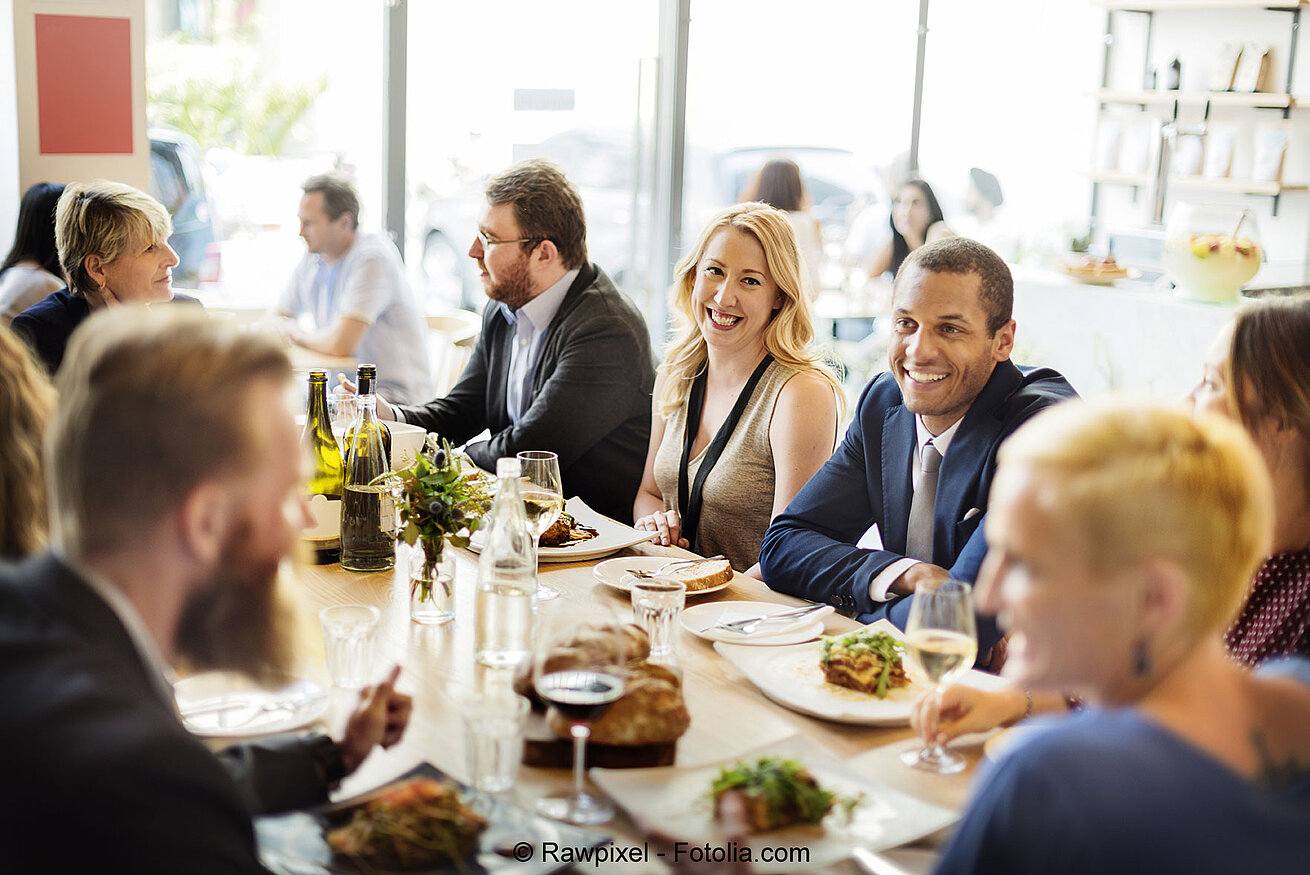 © Rawpixel - Fotolia Kollegen sitzen gemeinsam am Tisch bei einer Firmenfeier und genießen Essen in geselliger Atmosphäre