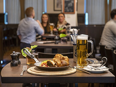 Rheinische Stov Servierter Schweinebraten mit Bier im Restaurant des Maritim Hotel Düsseldorf, im Hintergrund Gäste in geselliger Atmosphäre.