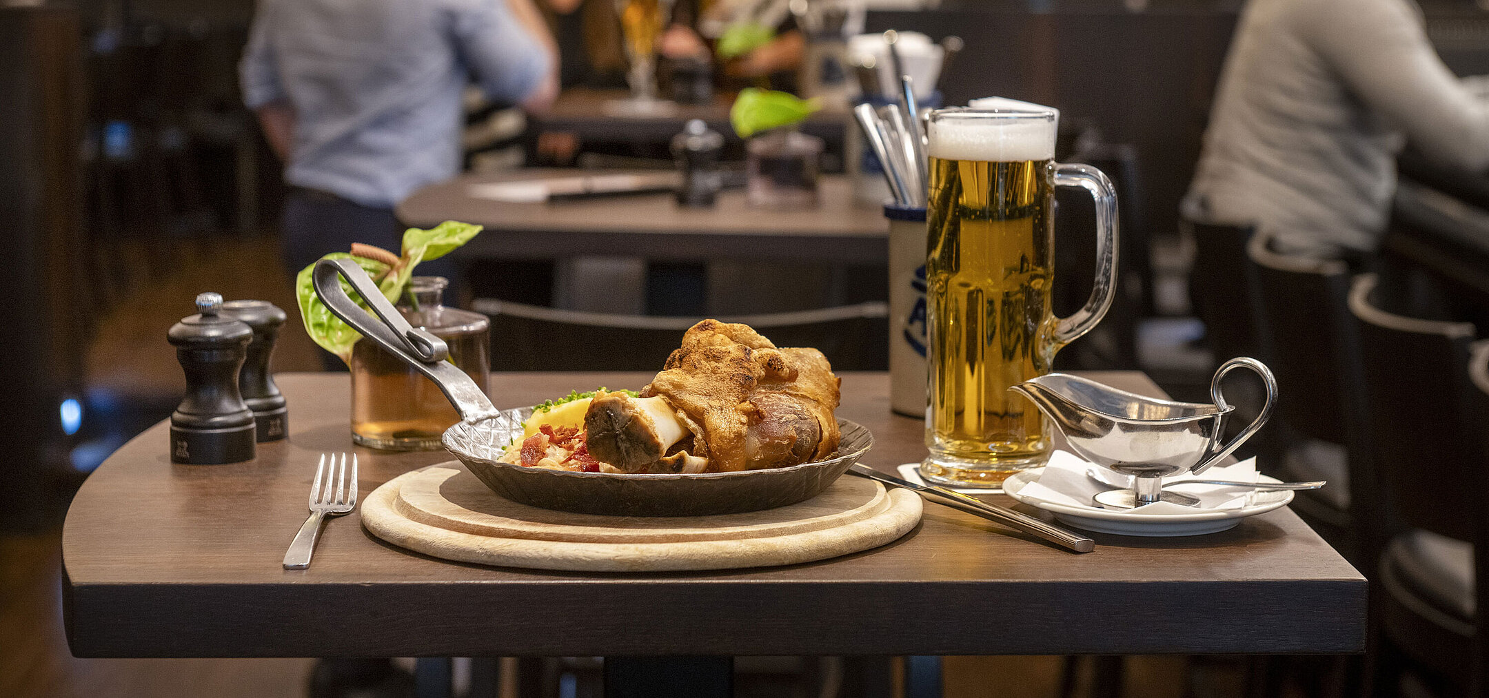 Servierter Schweinebraten mit Bier im Restaurant des Maritim Hotel Düsseldorf, im Hintergrund Gäste in geselliger Atmosphäre.
