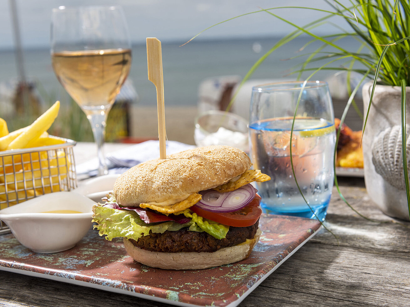 Burger mit Pommes, Salat und Getränken auf Holztisch in der Beach-Lounge vom Maritim Hotel Timmendorfer Strand.