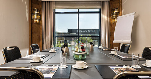 Heller Besprechungsraum mit Konferenztisch, Getränken und Blick auf den Flughafen im Maritim Hotel Hannover.