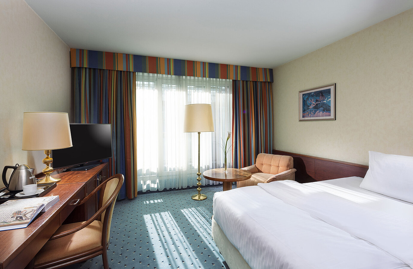 Helles Comfort Zimmer im Maritim Hotel Köln mit Einzelbett, Schreibtisch, Fernseher, Sessel und großen Fenstern mit Vorhängen