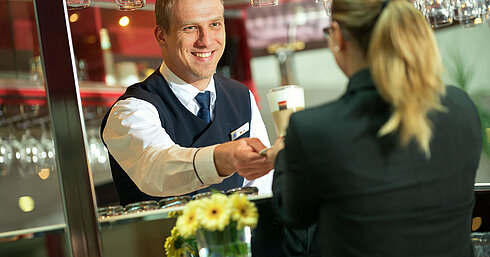 Ein Barkeeper reicht einem Gast ein Getränk an der Bar im Maritim Hotel mit lächelndem Service.