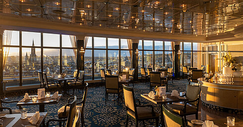 Restaurant im Maritim Hotel Ulm mit stilvollen Sitzplätzen, Panoramafenstern und Blick über Ulm bei Sonnenuntergang