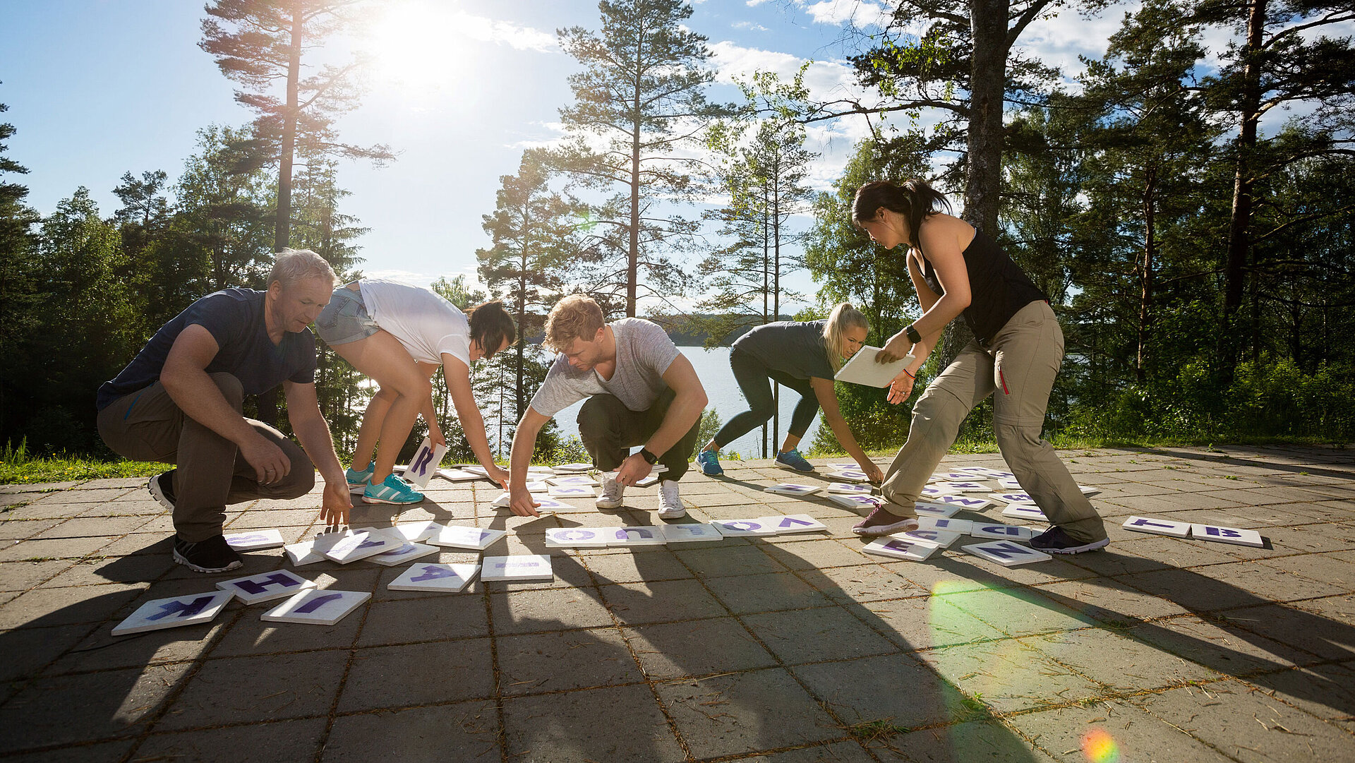 Gruppe von Erwachsenen beim Outdoor-Teambuilding macht gemeinsame Fitnessübung im Wald bei Sonnenschein