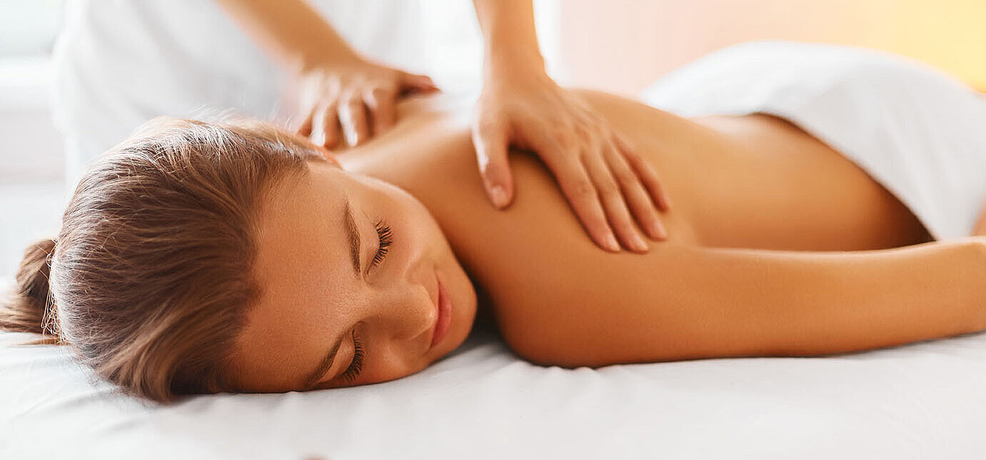 Frau genießt entspannende Rückenmassage im Spa mit warmem Licht und Steinen